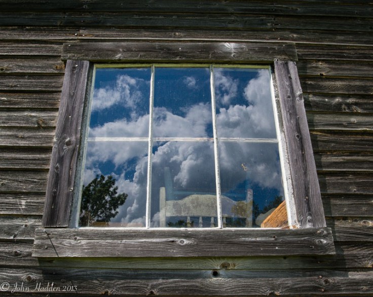 Fair weather cumulus clouds reflect in a weathered window.